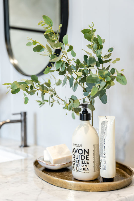 Compagnie de Provence Shea Butter liquid soap and hand cream on a brass tray with eucalyptus