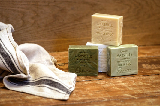 Lothantique Marseille soap bars (Olive, White Tea, Sweet Almond) stacked on a wooden table with striped linen