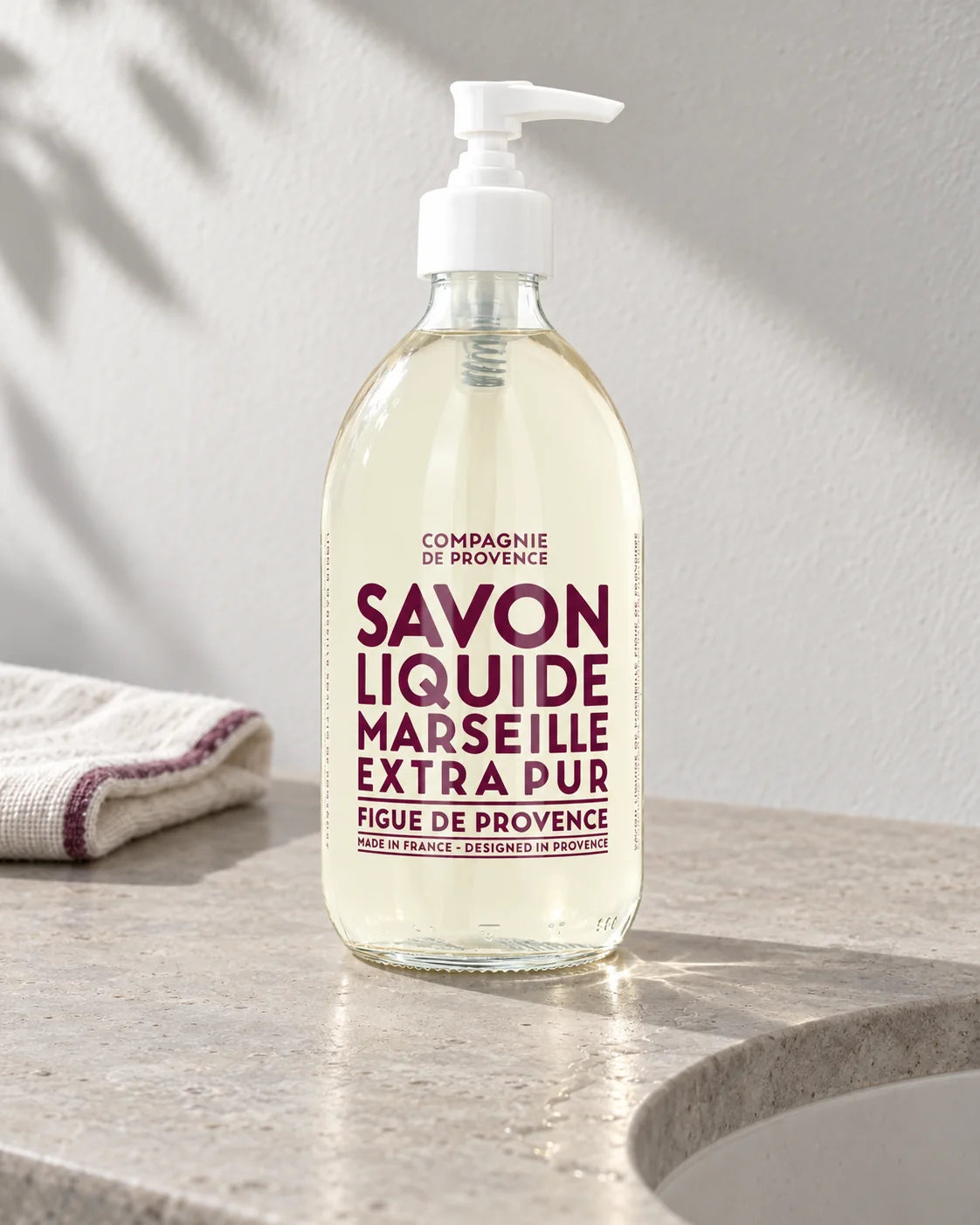 Compagnie de Provence Fig of Provence liquid soap, 495 ml, beside a pale stone basin in clear daylight; AI-styled setting